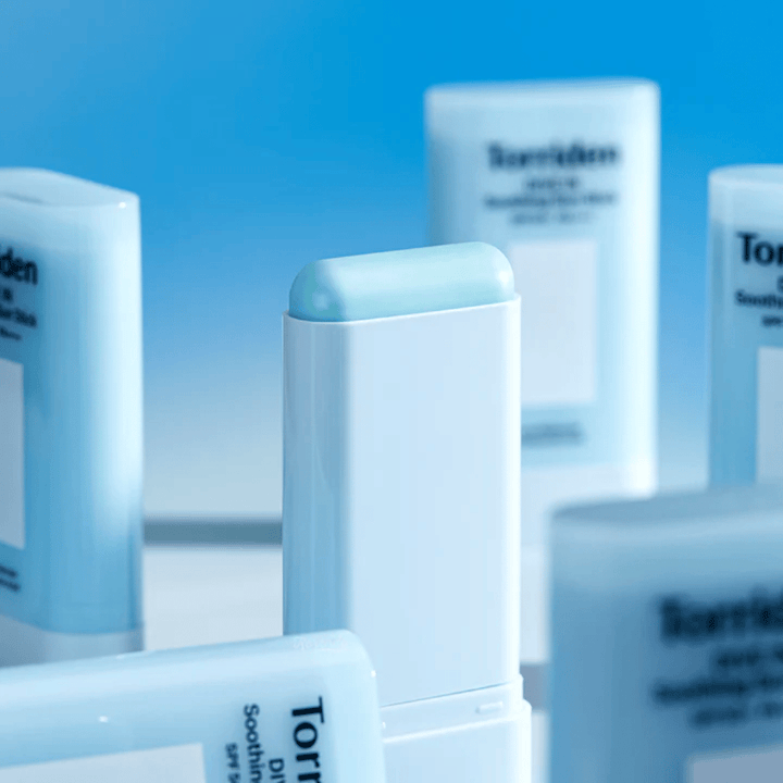 Zbliżenie na Torriden DIVE IN Soothing Sun Stick, pokazujące miękką formułę ochrony przeciwsłonecznej w sztyfcie, z kilkoma produktami w tle.
