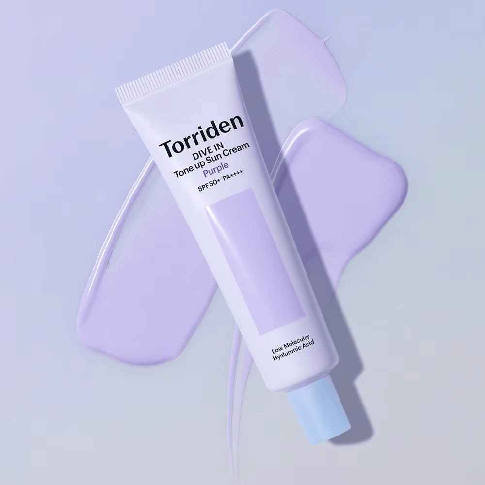 Torriden DIVE IN Tone Up Sun Cream Purple umieszczony na rozsmarowanym fioletowym kremie, który podkreśla efekt wyrównania kolorytu i nadania blasku.