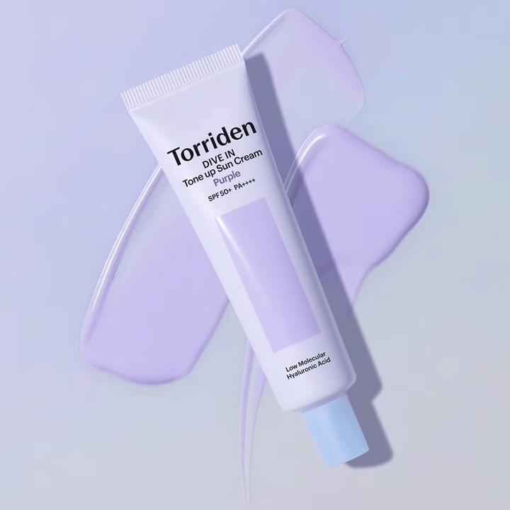 Torriden DIVE IN Tone Up Sun Cream Purple umieszczony na rozsmarowanym fioletowym kremie, który podkreśla efekt wyrównania kolorytu i nadania blasku.