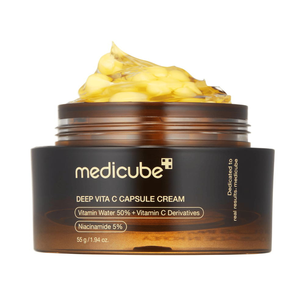 Zbliżenie "Medicube Deep Vita C Capsule Cream", pokazujące konsystencję kremu i kapsułki witaminy C. Opakowanie jest ciemnobrązowe ze złotym tekstem i opisuje zawartość wody witaminowej (50%) i niacynamidu (5%), co daje wizualną prezentację nawilżających i poprawiających skórę właściwości produktu.
