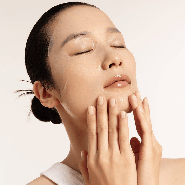 Modelka z nawilżoną i promienną skórą nakłada Maseczka w płachcie, skupienie na blasku, równym kolorycie skóry i połysku.