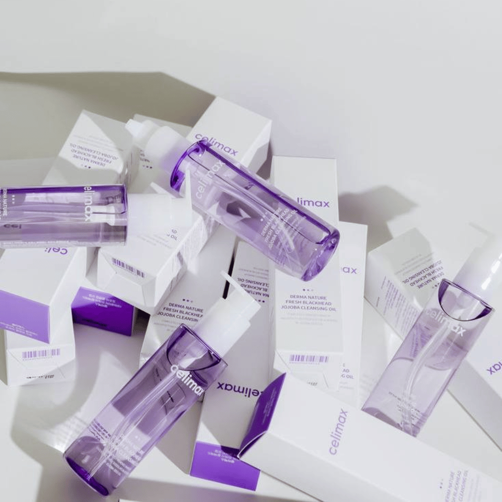 Celimax Derma Nature Fresh Blackhead Jojoba Cleansing Oil w fioletowych butelkach umieszczone wśród białych opakowań z fioletowymi detalami.