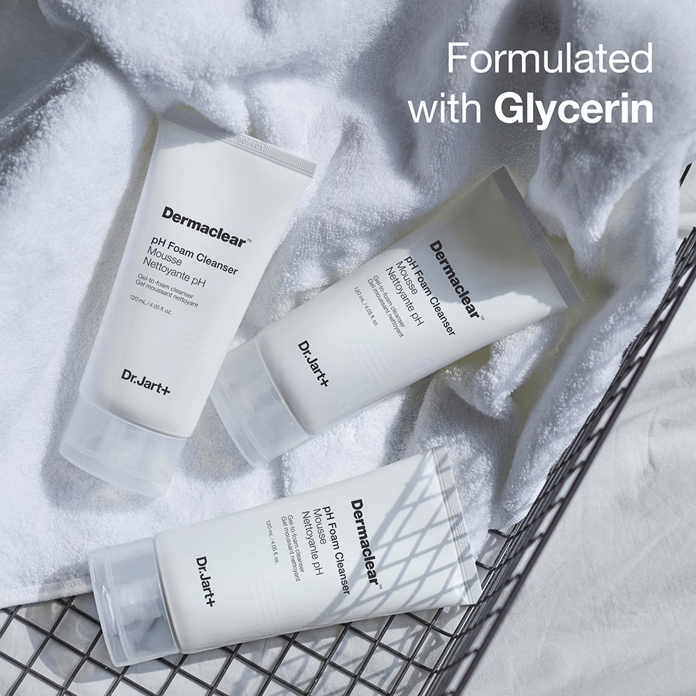 Trzy tuby Dr.Jart+ Dermaclear pH Foam Cleanser leżą na białym ręczniku frotte w metalowym koszu, z tekstem "Formulated with Glycerin" w górnym rogu.