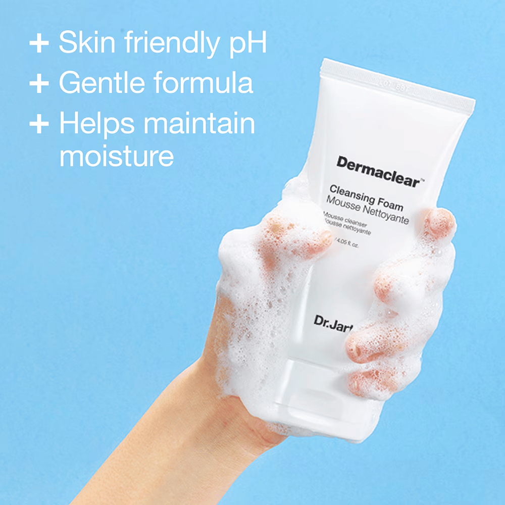 Ręka pokryta pianą trzyma Dr.Jart+ Dermaclear Cleansing Foam na niebieskim tle, z tekstem podkreślającym przyjazne dla skóry pH, łagodną formułę i właściwości nawilżające.