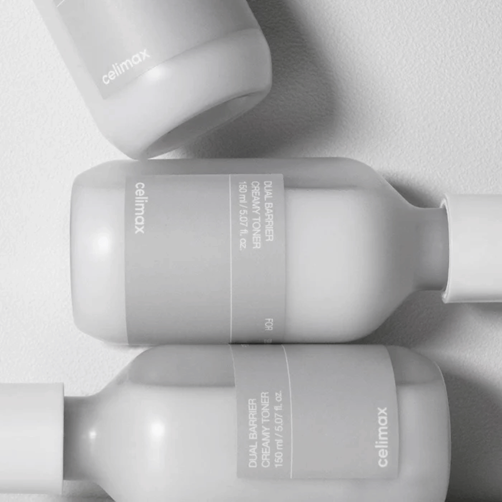 Trzy leżące butelki Celimax Dual Barrier Creamy Toner w minimalistycznym designie z szarą etykietą i miękkim światłem – idealne dla skóry wrażliwej i suchej.