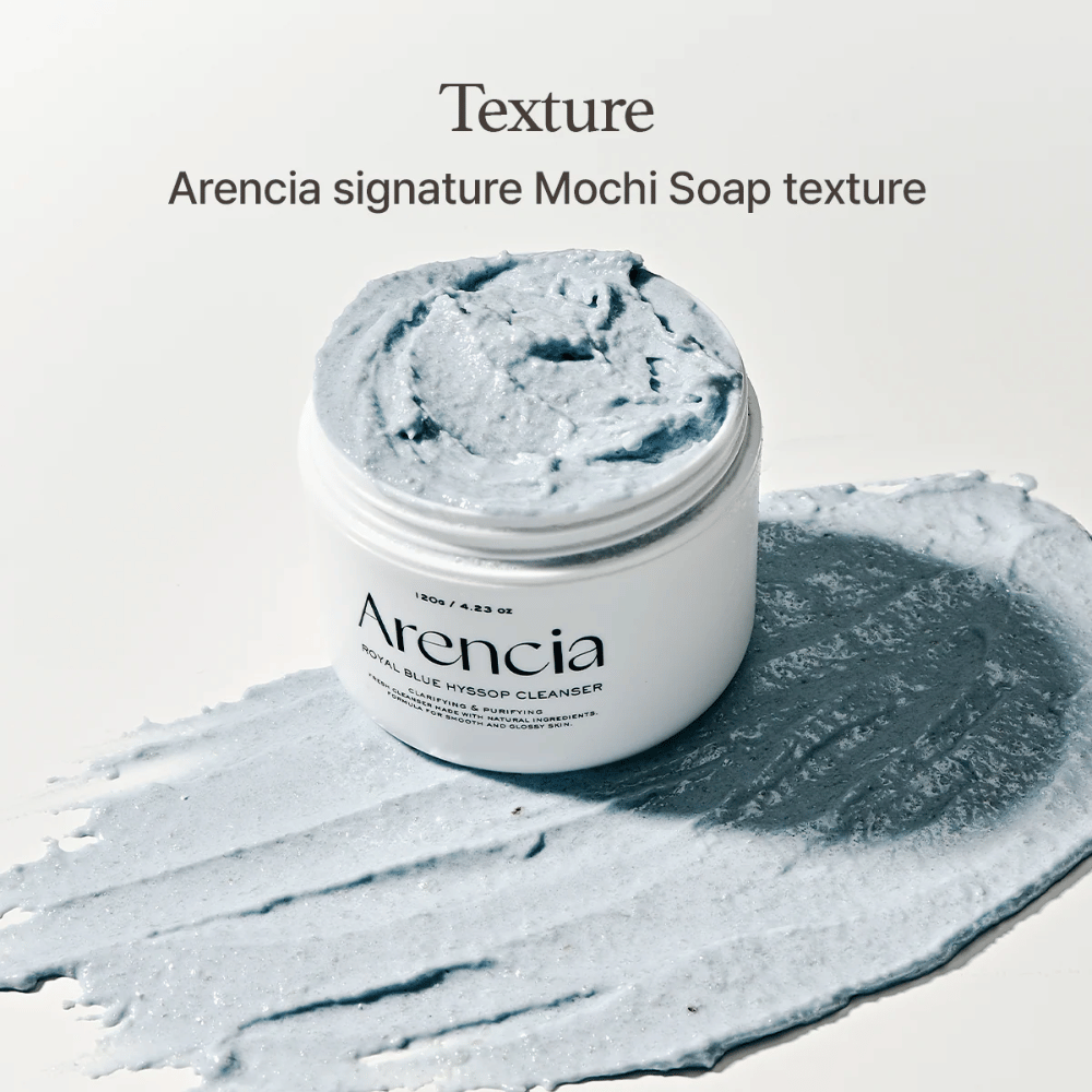 Otwarty słoik z Arencia Fresh Blue Hyssop Rice Mochi Cleanser, umieszczony na rozsmarowanej warstwie niebieskiej, kremowej formuły czyszczącej, która ukazuje swoją mochi-podobną teksturę.