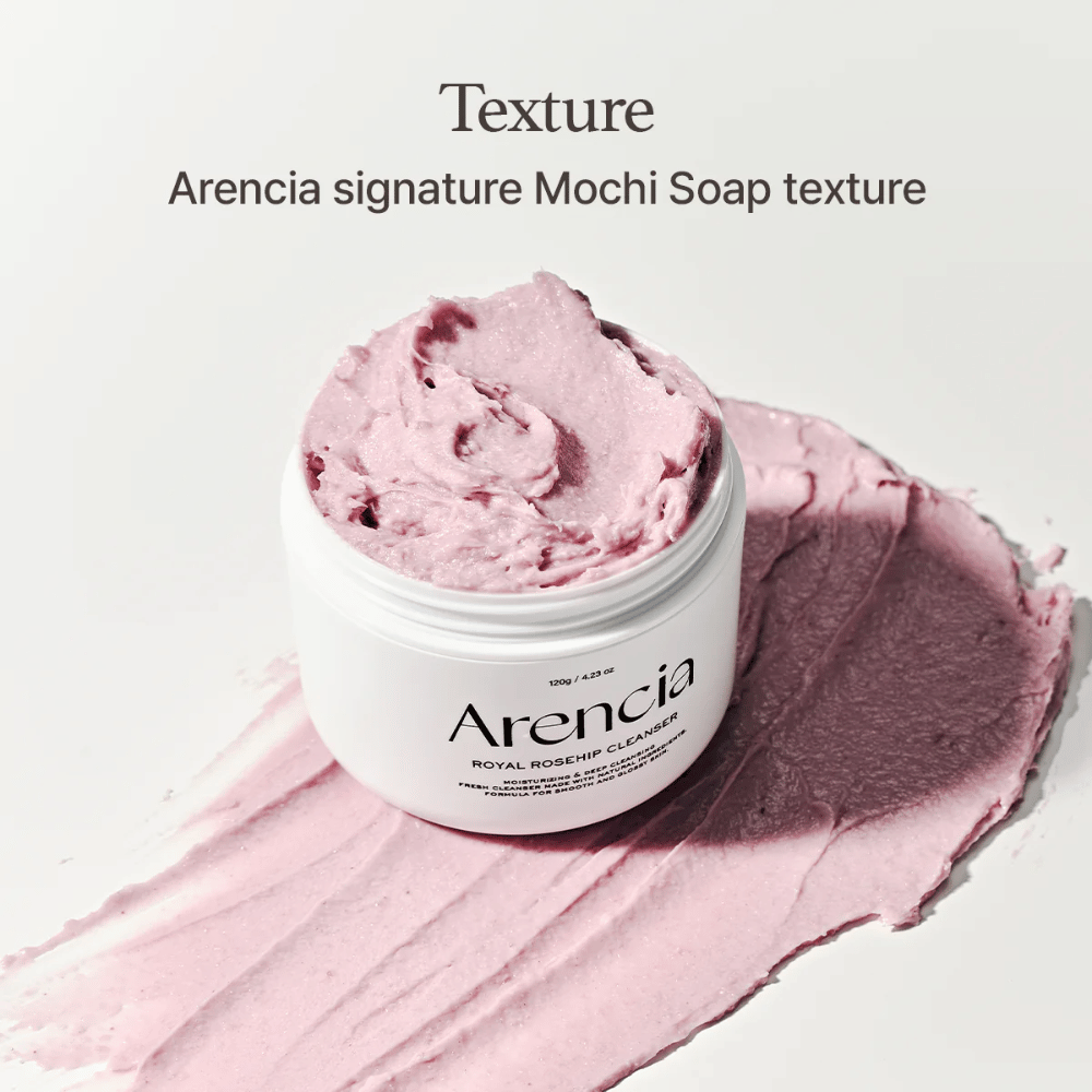 Słoik z Arencia Royal Rosehip Cleanser widoczny na rozsmarowanym różowym oczyszczaczu o mochi-podobnej konsystencji. Tekst powyżej opisuje produkt jako sygnaturową teksturę Arencji.