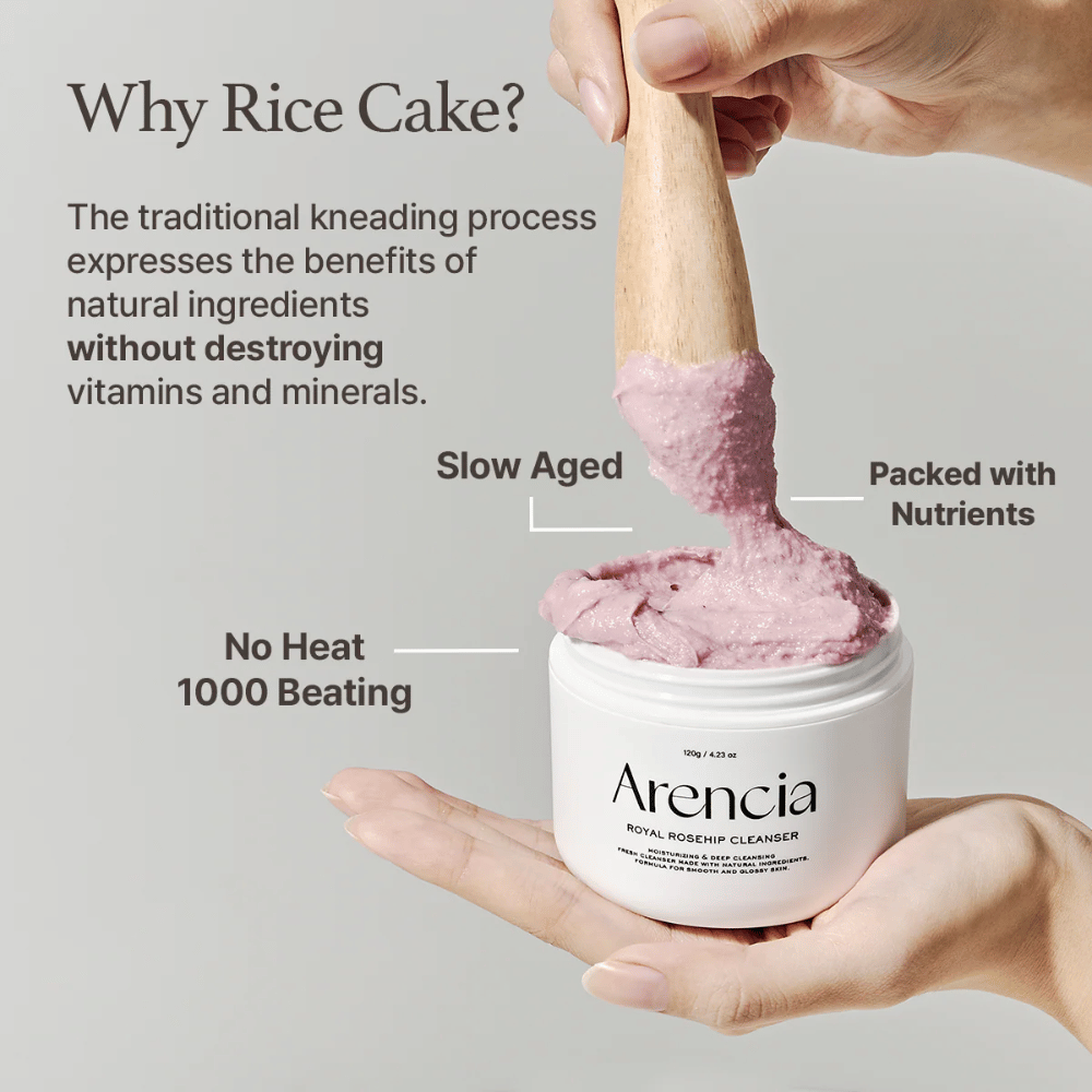 Ręka trzyma otwarty słoik Arencia Royal Rosehip Cleanser, z różową, mochi-podobną formułą oczyszczającą podnoszoną drewnianą szpatułką – pokazuje teksturę produktu i tradycyjną metodę produkcji.