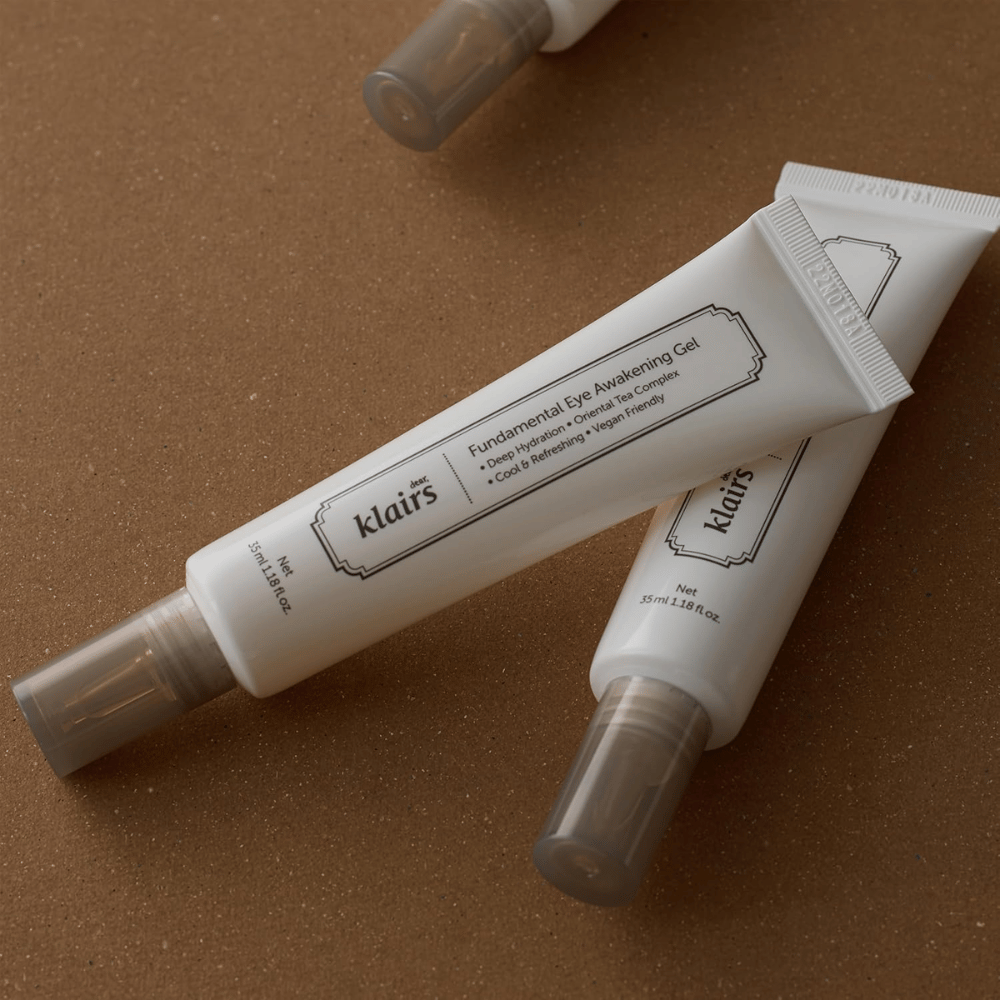 Zdjęcie lifestyle’owe z dwiema tubkami Klairs Fundamental Eye Awakening Gel umieszczonymi na ciepłym brązowym tle. Kompozycja podkreśla elegancki design produktu i jego premium charakter, jednocześnie skupiając uwagę na pielęgnacji okolic oczu i nawilżeniu.