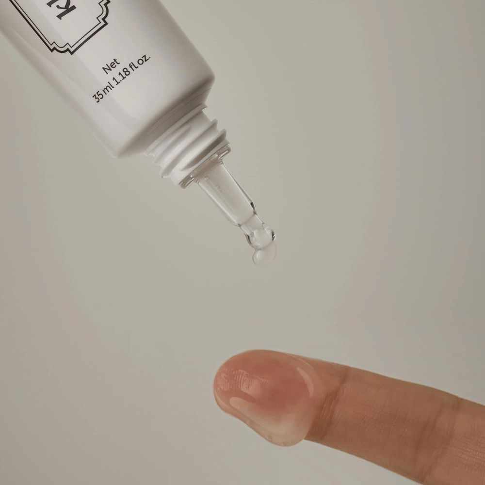 Zbliżenie, na którym przejrzysty, lekki żel jest aplikowany z wąskiej końcówki na palec. Obraz ilustruje transparentną, żelową konsystencję produktu oraz precyzyjną aplikację wokół okolic oczu.