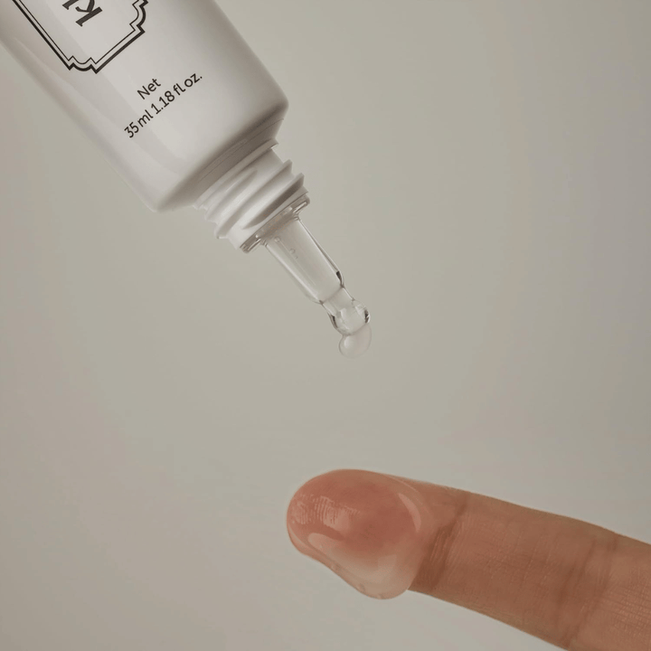 Zbliżenie, na którym przejrzysty, lekki żel jest aplikowany z wąskiej końcówki na palec. Obraz ilustruje transparentną, żelową konsystencję produktu oraz precyzyjną aplikację wokół okolic oczu.