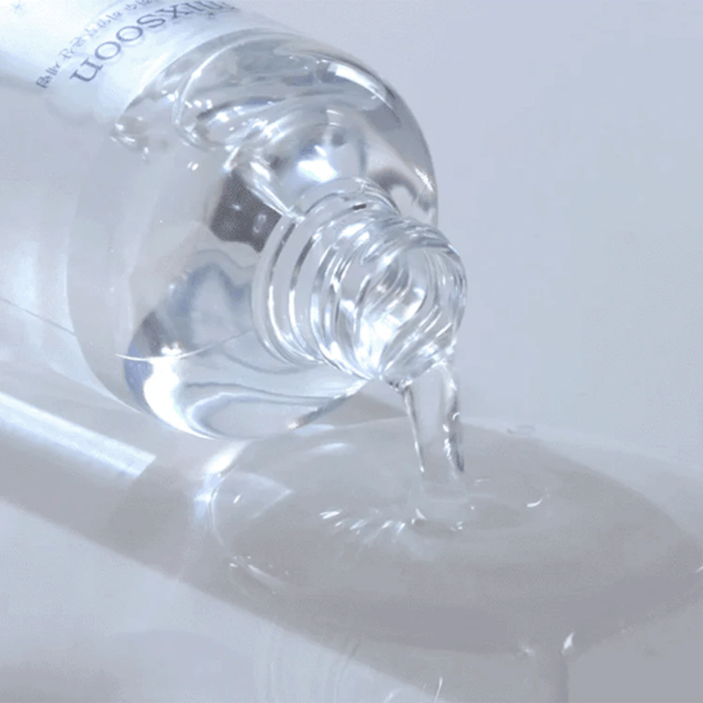 Zbliżenie na przezroczyste serum wylewane z butelki Mixsoon Glacier Water Hyaluronic Acid Serum na błyszczącą powierzchnię.