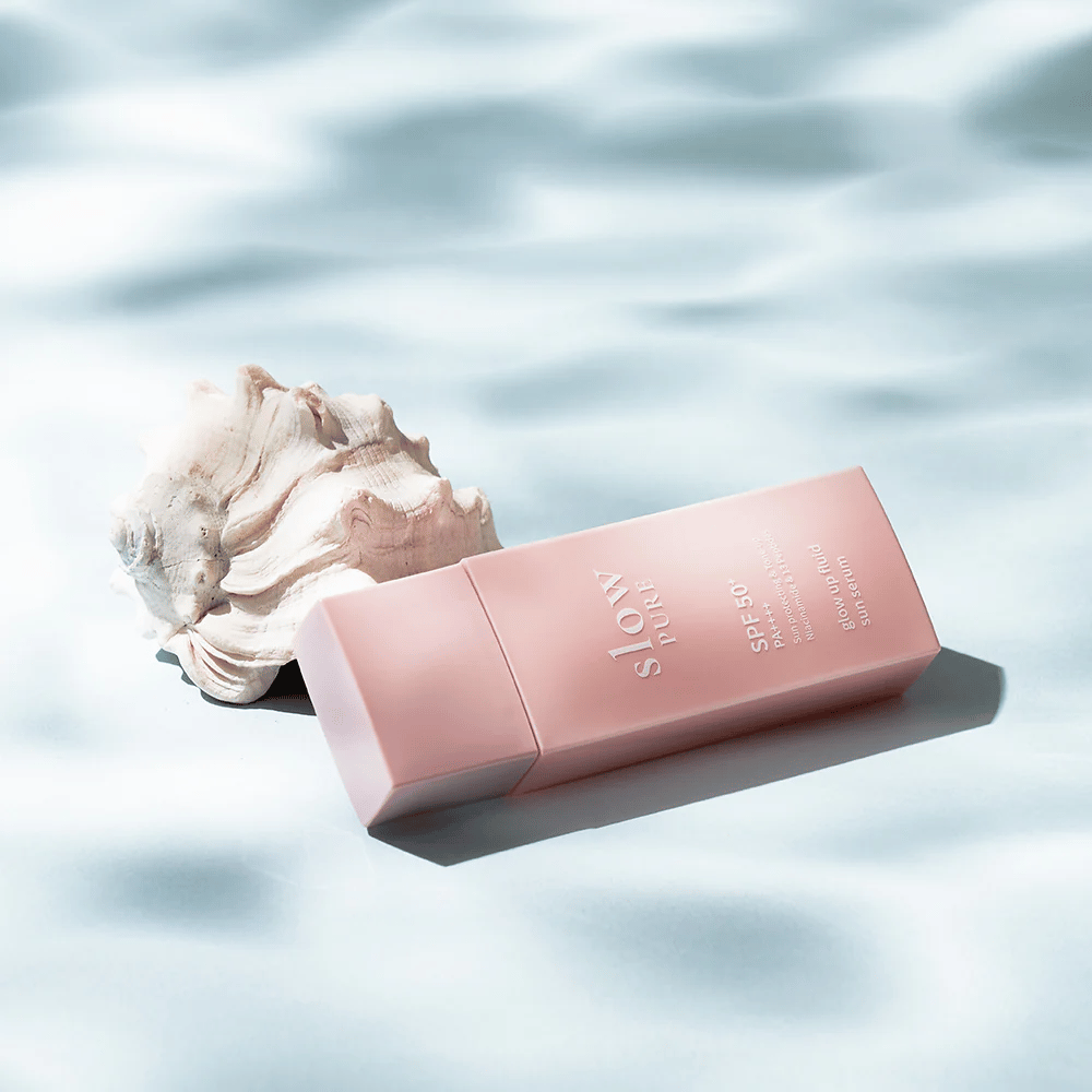 Slow Pure Glow Up Fluid Sun Serum przy muszli i efekcie wodnym, podkreśla ochronę przeciwsłoneczną i blask.