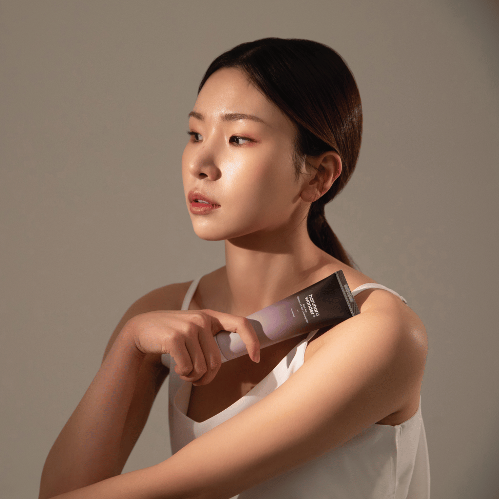 Młoda azjatycka kobieta trzymająca szczotkę w ręku podczas używania Haruharu Wonders Black Rice Moisture 5.5 Soft Cleansing Gel 100ml.