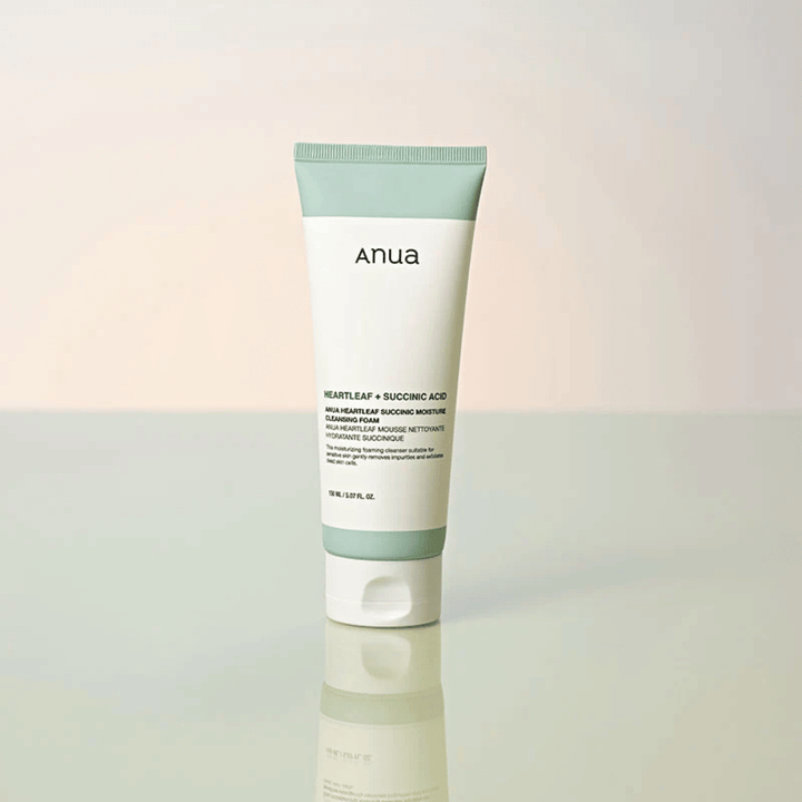 Samodzielne zdjęcie produktu Anua Heartleaf + Succinic Acid Moisture Cleansing Foam. Produkt jest pokazany w pozycji stojącej na odbijającej światło powierzchni, która wyraźnie podkreśla design opakowania i elegancką estetykę marki.