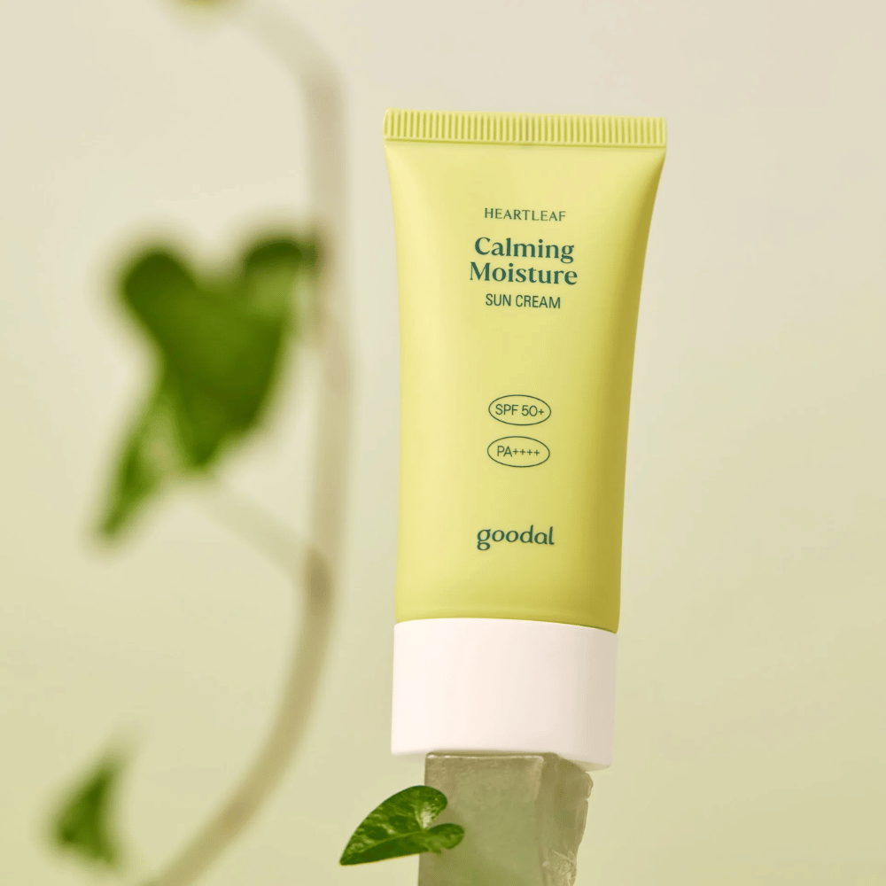 Goodal Heartleaf Calming Moisture Sun Cream SPF50+ PA++++ umieszczony na szklanej powierzchni z zieloną rośliną w tle – kojący krem przeciwsłoneczny dla wrażliwej skóry.