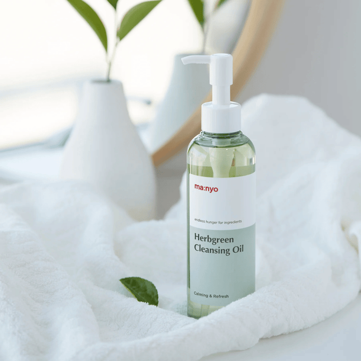 ma:nyo Herbgreen Cleansing Oil w butelce z pompką umieszczoną na białym ręczniku, kojący olejek oczyszczający z ziołowymi składnikami do delikatnego oczyszczania twarzy