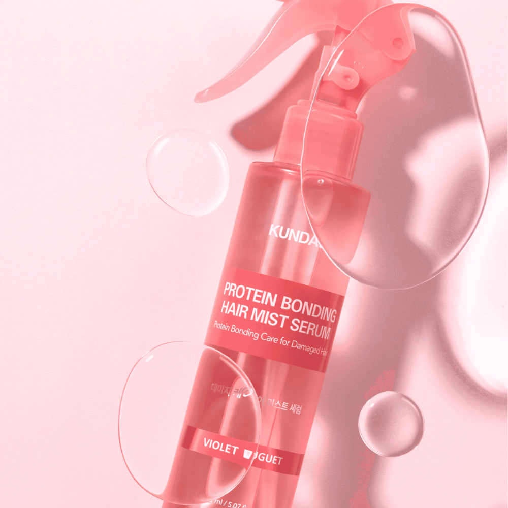 KUNDAL Protein Bonding Hair Mist Serum Violet Bouquet w różowej butelce z rozpylaczem, sfotografowane na różowym tle z kroplami wody.