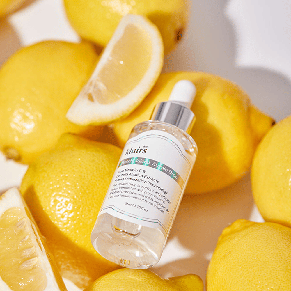 Klairs Freshly Juiced Vitamin Drop butelka serum otoczona świeżymi połówkami cytryn i plasterkami cytryny na jasnej powierzchni, podkreślając składniki.