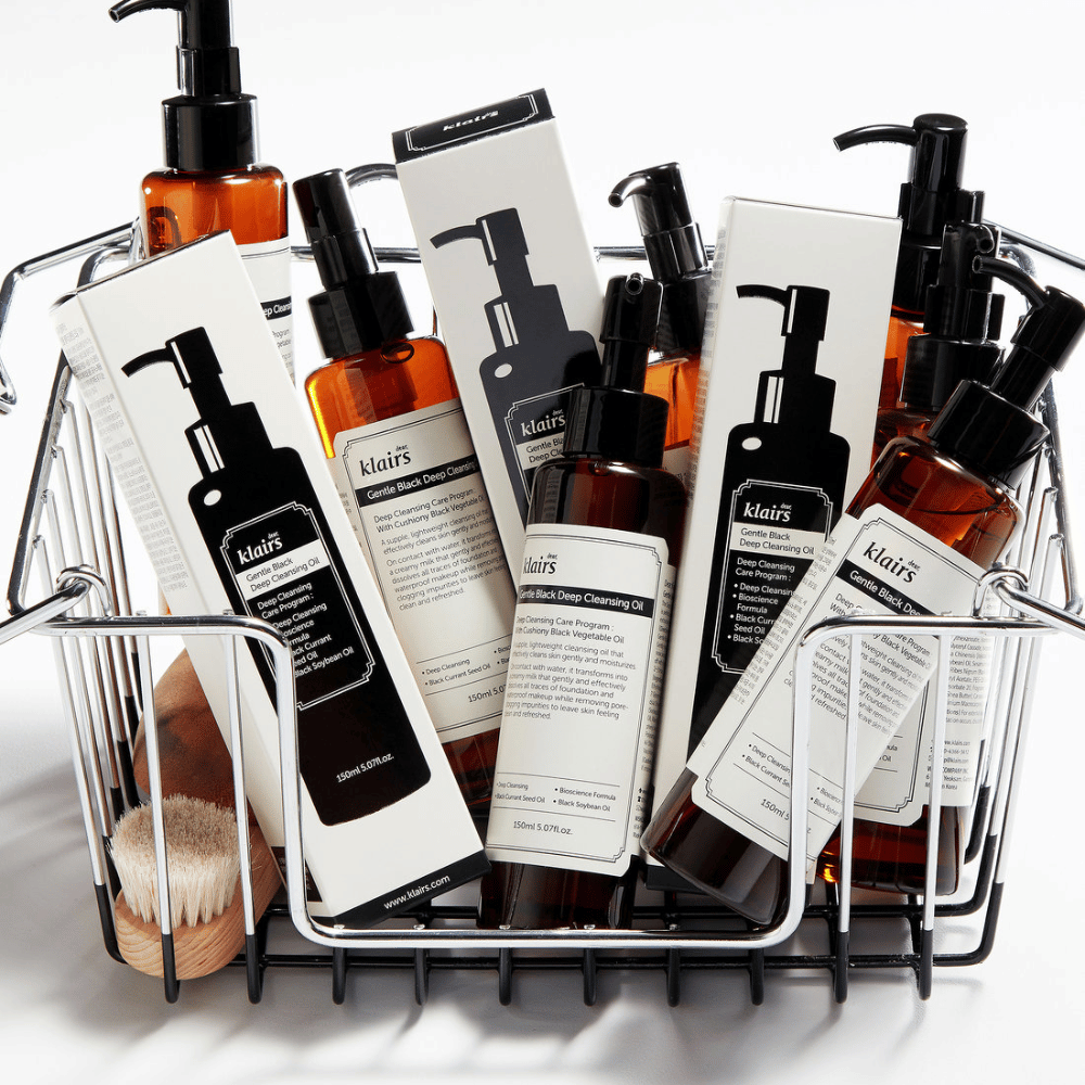 Miniwózek na zakupy wypełniony produktami do pielęgnacji skóry od Klairs, w tym Gentle Black Deep Cleansing Oil w przezroczystych butelkach z czarnymi pompkami i pasującymi opakowaniami.
