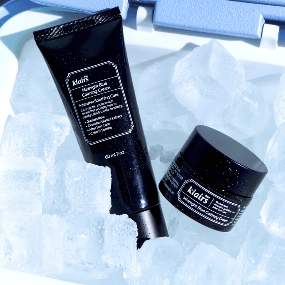 Tubka i słoiczek Klairs Midnight Blue Calming Cream leżą na kostkach lodu, z naciskiem na właściwości kojące i nawilżające, na niebieskim tle.