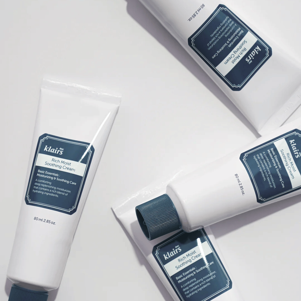 Kilka tubek Klairs Rich Moist Soothing Cream strategicznie rozmieszczonych na jasnej powierzchni, z cieniami tworzącymi głębię.