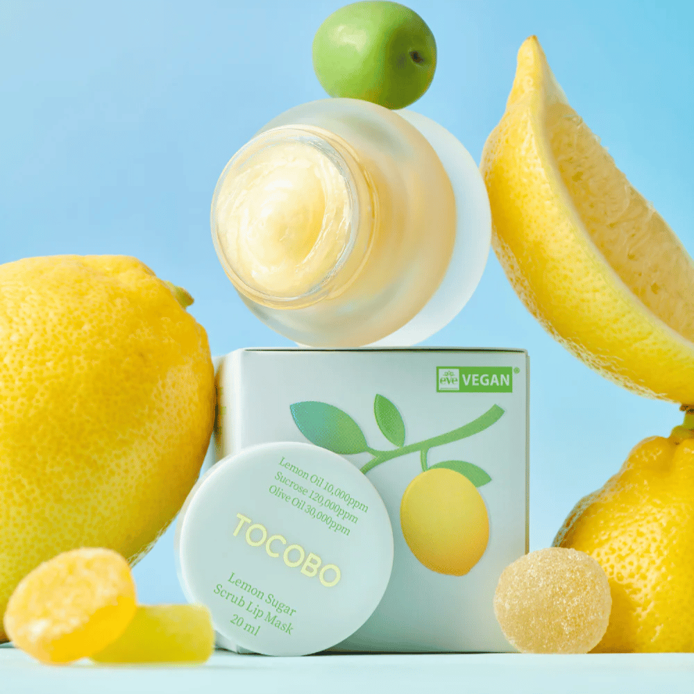 Słoik z Tocobo Lemon Sugar Scrub Lip Mask umieszczony wśród cytryn i opakowania, oznaczony jako przyjazny dla wegan.