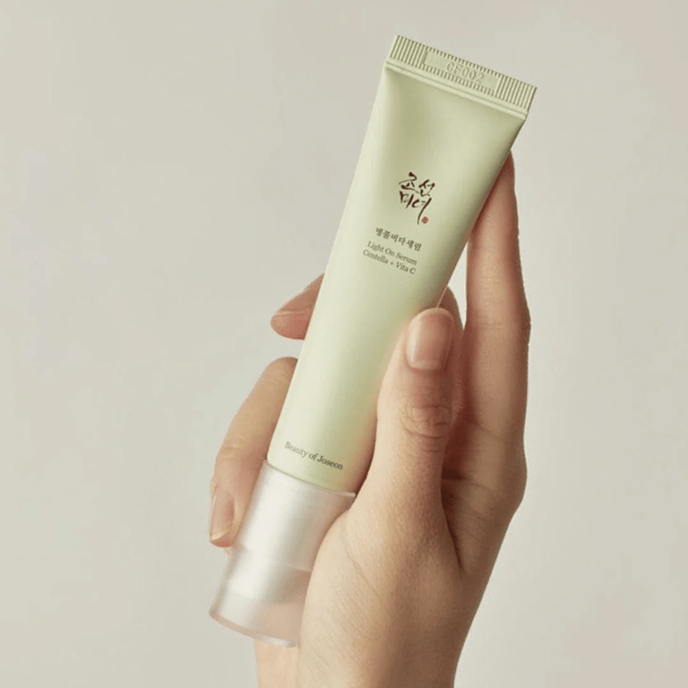 Ręka trzyma Beauty of Joseon Light On Serum z Centellą i witaminą C, w jasnozielonej tubce o minimalistycznym designie na neutralnym tle.