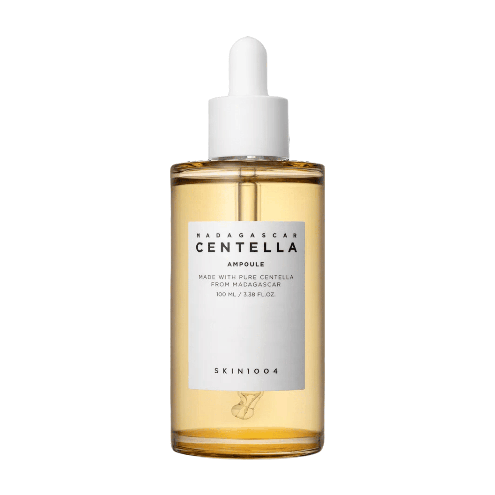 Obraz przedstawia butelkę z "Madagascar Centella Asiatica 100 Ampoule" od SKIN1004. Butelka zawiera 100 ml i twierdzi, że jest wykonana z czystej centelli z Madagaskaru. Produkt wygląda na serum do pielęgnacji skóry, a prosta etykieta daje wrażenie czystości i naturalności. Butelka z zakraplaczem sugeruje, że jest to starannie dawkowany produkt do pielęgnacji skóry.