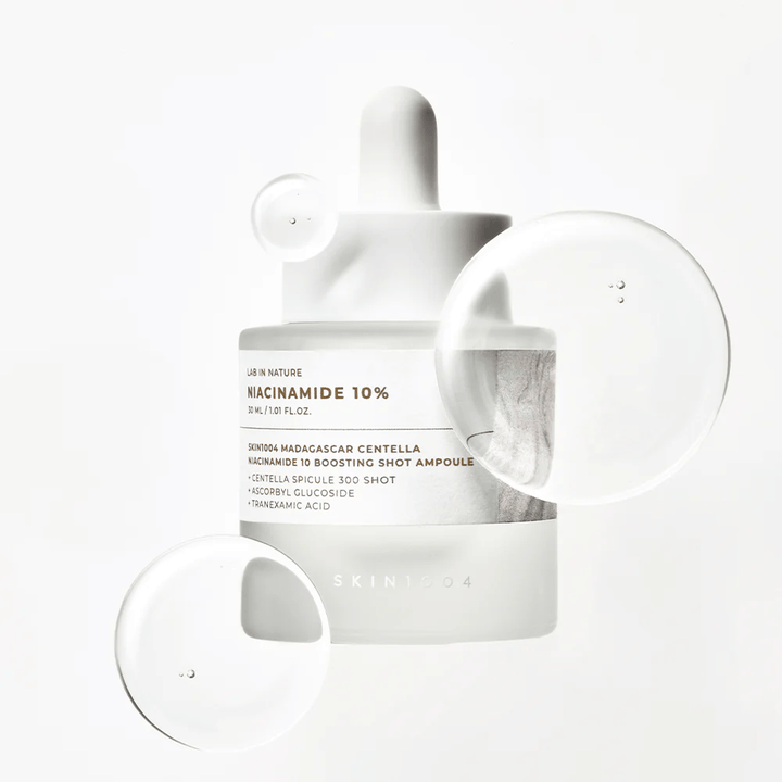 SKIN1004 Madagascar Centella Niacinamide 10 Boosting Shot Ampoule z kroplami serum pokazującymi lekką, szybko wchłaniającą się formułę z niacynamidem, kwasem traneksamowym i wąkrotą.