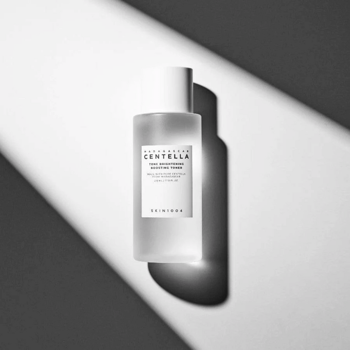 Flaska av SKIN1004 Madagascar Centella Tone Brightening Boosting Toner liggande på vit yta med dramatisk skugga i svartvitt ljusspel.