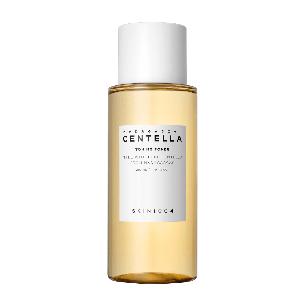 Obraz przedstawia butelkę z tonikiem do pielęgnacji skóry, oznaczoną "Madagascar Centella Toning Toner" od SKIN1004. Produkt podano, że zawiera 210 ml lub 7.10 fl.oz i jest wytwarzany z czystej Centelli z Madagaskaru. Opakowanie jest proste i eleganckie z przezroczystą butelką i złotym tonikiem wewnątrz, co daje poczucie luksusu i czystości. Logo marki SKIN1004 jest wyraźnie widoczne w dolnej części etykiety.
