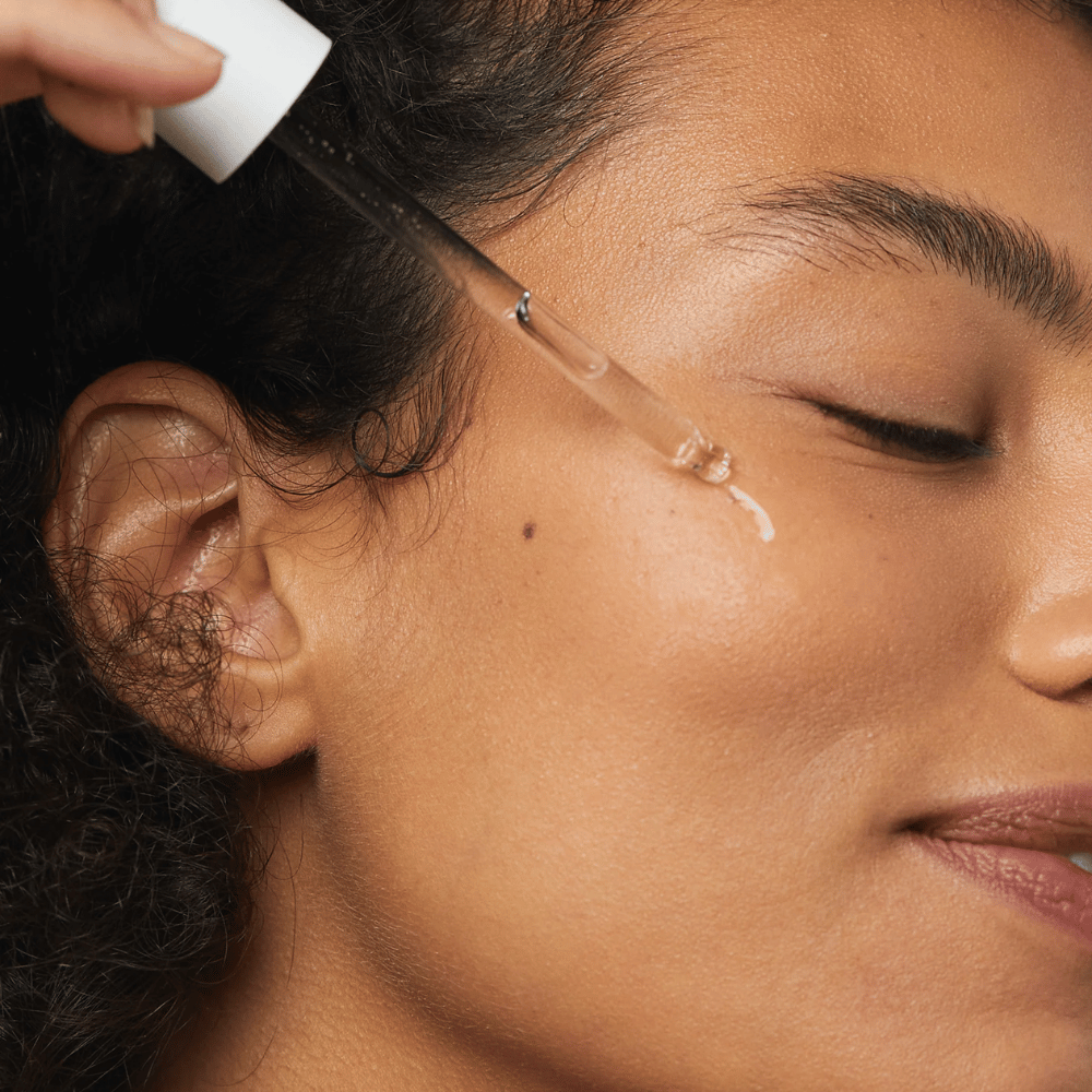 Kobieta nakłada Skin1004 Madagascar Centella Hyalu-Cica First Ampoule na policzek za pomocą pipety.