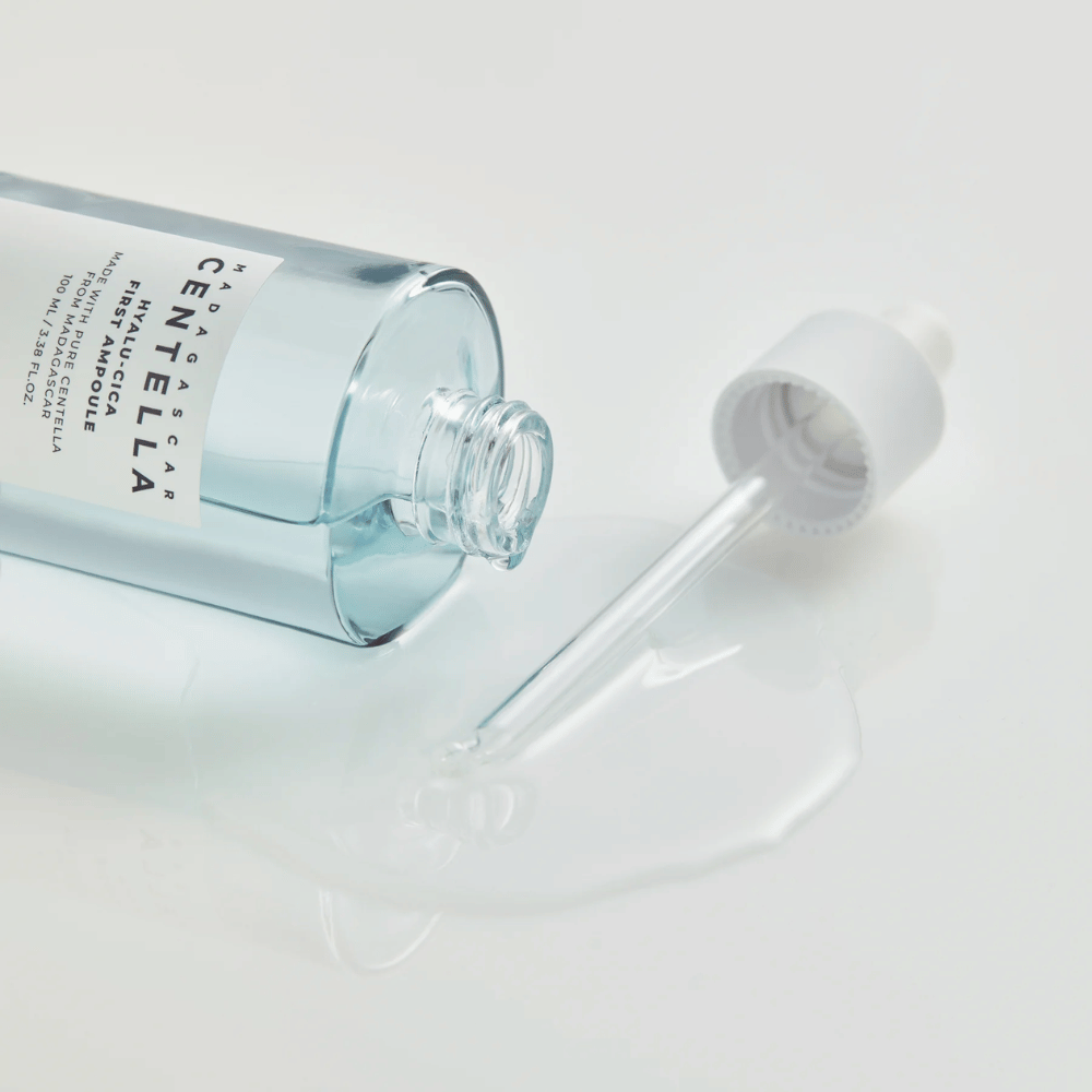 Zbliżenie na otwartą butelkę Skin1004 Madagascar Centella Hyalu-Cica First Ampoule z pipetą leżącą i serum rozlanym na białej powierzchni.