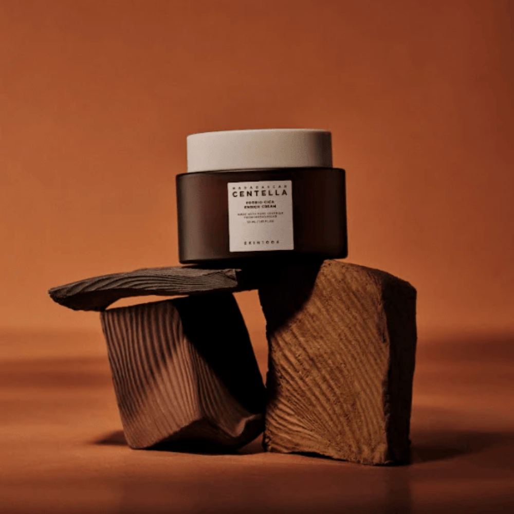 SKIN1004 Madagascar Centella Probio-Cica Enrich Cream w eleganckim brązowym słoiku na dekoracyjnych drewnianych blokach – odżywczy koreański krem do twarzy wzmacniający barierę ochronną skóry.