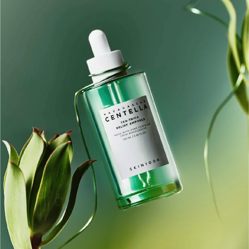 SKIN1004 Madagascar Centella Tea-Trica Relief Ampoule – zielona szklana butelka z pipetą, białą etykietą i zawartością 100 ml, sfotografowana na zielonym tle z detalami roślinnymi.