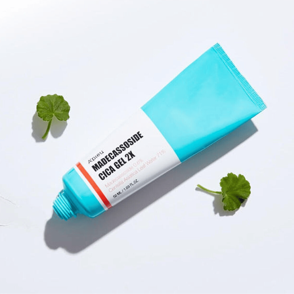 A’pieu Madecassoside Cica Gel 2X w niebieskiej tubce z białą etykietą, otoczona trzema zielonymi liśćmi centella asiatica na białym tle.