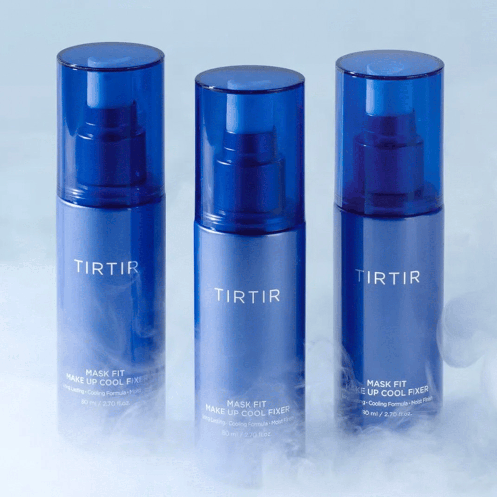 Trzy niebieskie butelki z rozpylaczem z etykietą "TIRTIR Mask Fit Make Up Cool Fixer". Każda butelka mieści 80 ml (2,70 fl. oz.) i jest zaprojektowana, aby zapewnić uczucie orzeźwienia i długotrwały makijaż. Butelki stoją na jasnym tle z mgłą, aby stworzyć atmosferę świeżości.