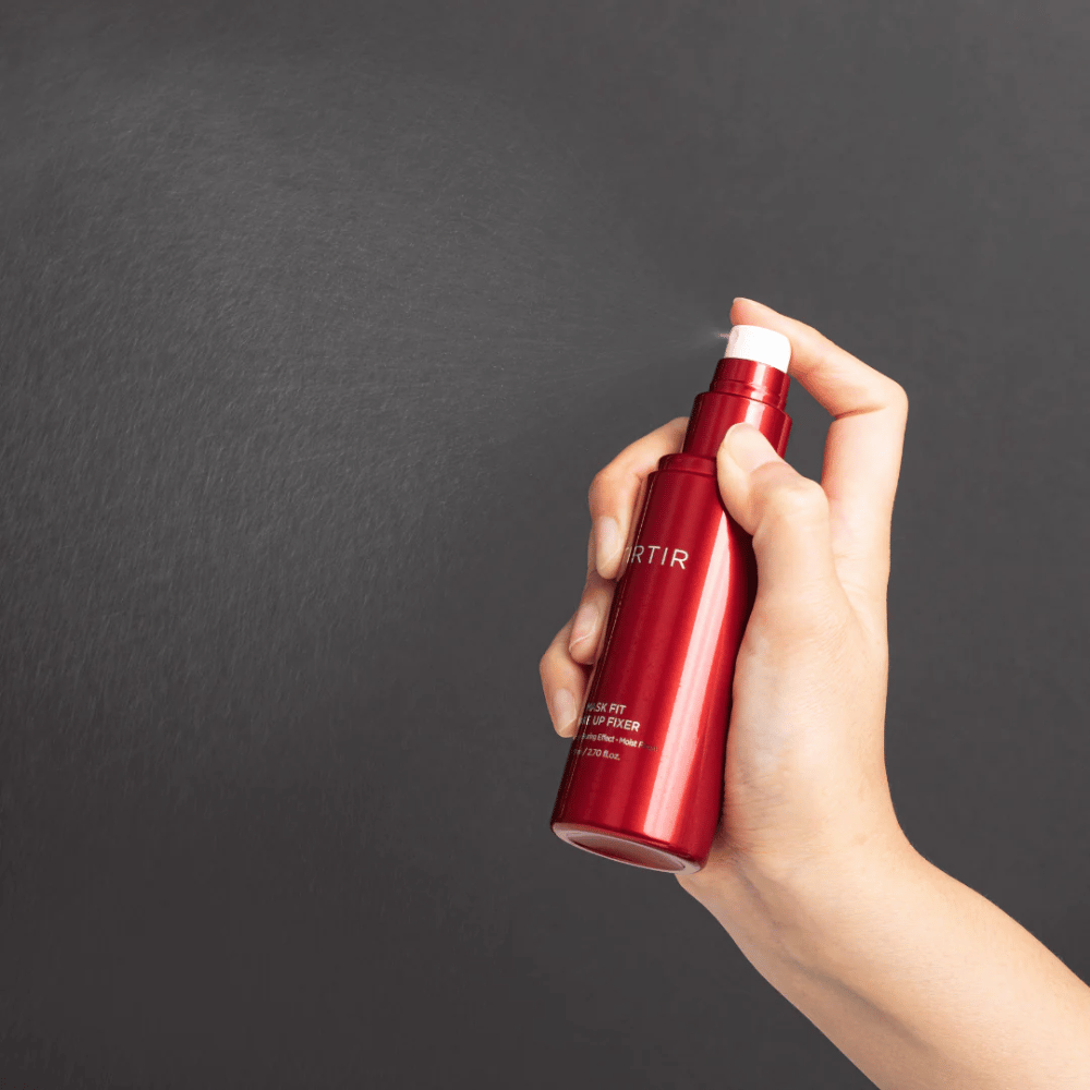 Ręka trzymająca czerwoną butelkę marki tirtir Mask Fit Make Up Fixer i rozpylająca delikatną mgiełkę, idealną do utrwalania makijażu.