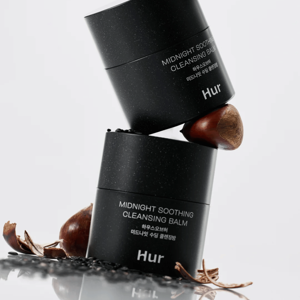 Dwa słoiki Jak Midnight Soothing Cleansing Balm ułożone z naturalnymi składnikami. Odżywczy balsam oczyszczający do codziennego oczyszczania wrażliwej skóry.