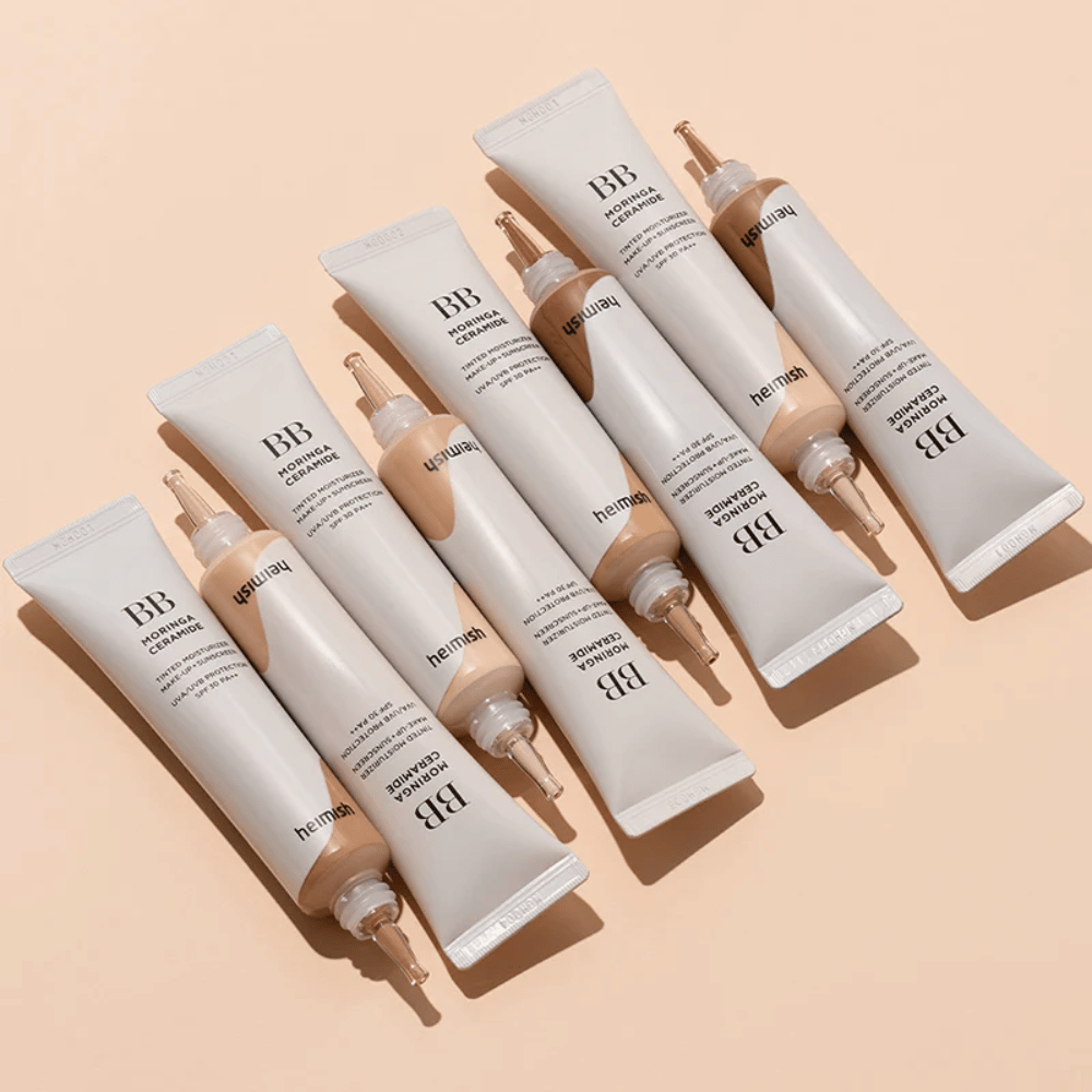 Kilka tubek Heimish Moringa Ceramide BB Cream ułożonych na jasnobeżowym tle. Obraz podkreśla różne odcienie oraz elegancki, minimalistyczny design opakowania produktu.