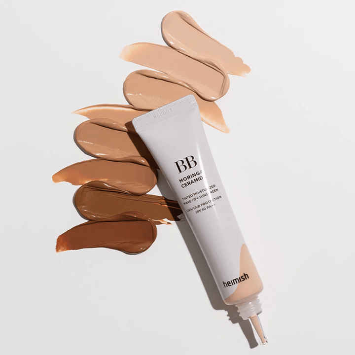 Heimish Moringa Ceramide BB Cream otoczony kilkoma próbkami odcieni w różnych tonacjach skóry. Obraz pokazuje szeroką gamę kolorystyczną produktu oraz kremową konsystencję, która zapewnia naturalne krycie i wyrównany koloryt skóry.