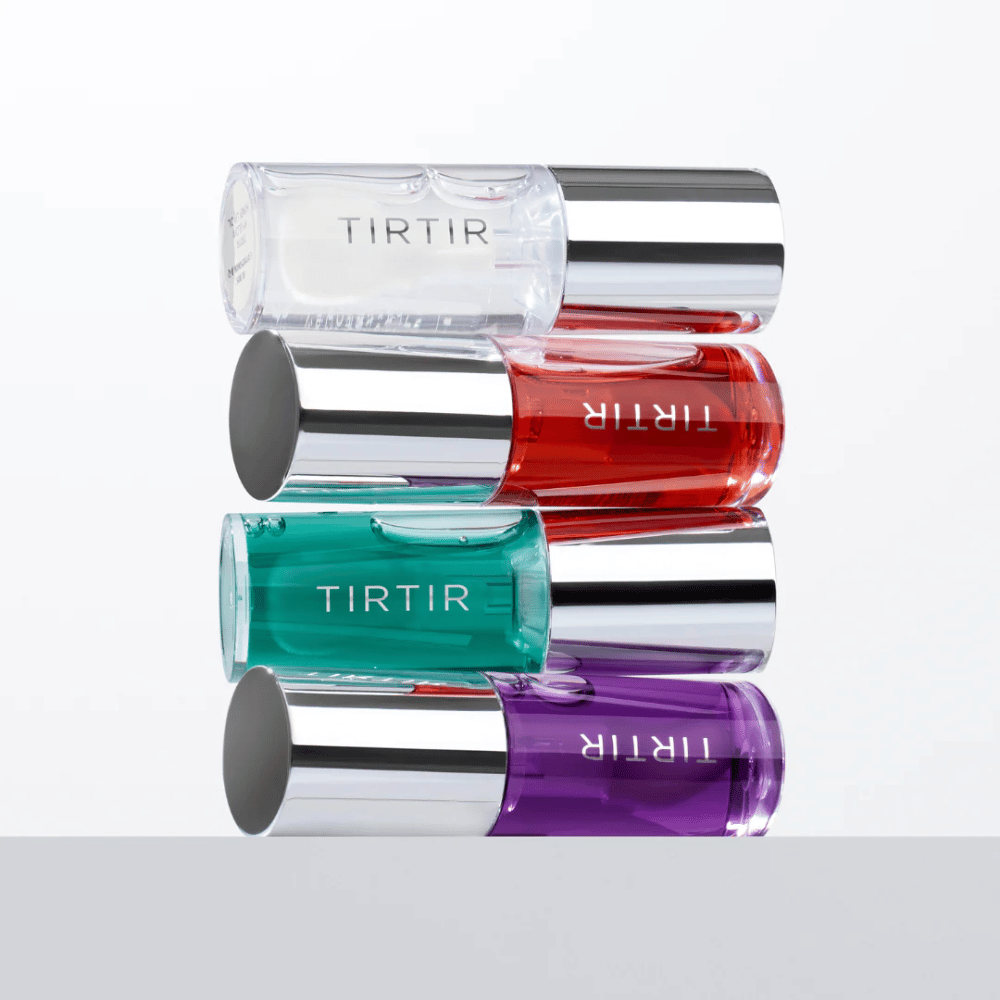 Cztery TIRTIR My Glow Lip Oil w różnych kolorach – przezroczystym, czerwonym, zielonym i fioletowym – ułożone jeden na drugim z srebrnymi nakrętkami na białym tle.