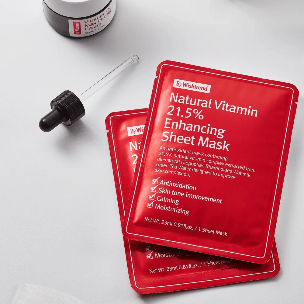 By Wishtrend Natural Vitamin 21.5% Enhancing Maseczka w płachcie w czerwonych opakowaniach, umieszczonych na białej powierzchni razem z pipetą i słoikiem kremu do twarzy.