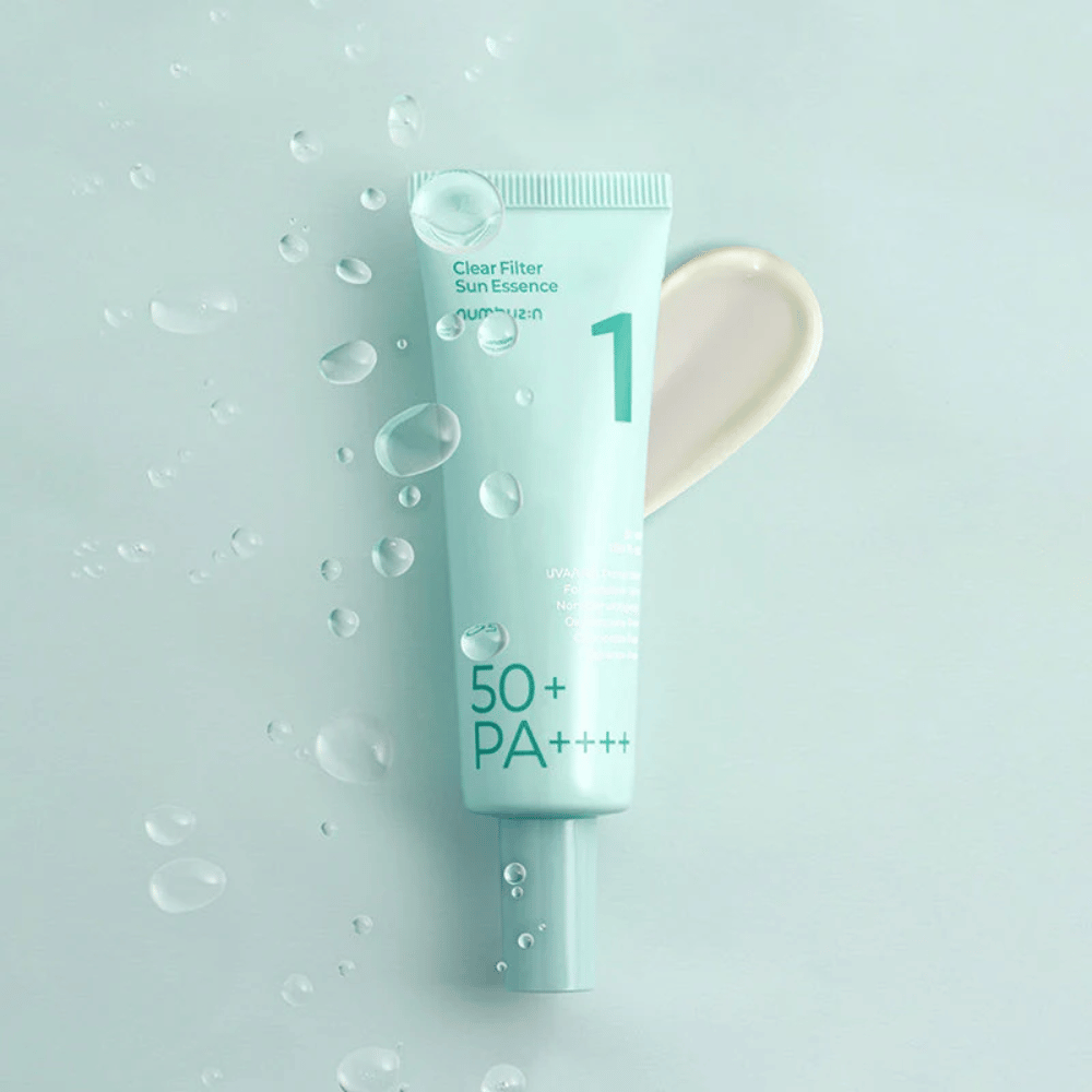 Jasnoniebieska tubka z No.1 Clear Filter Sun Essence SPF 50+ PA++++. Tubka jest ozdobiona kroplami wody, a obok pokazana jest porcja produktu. Produkt jest zaprojektowany, aby zapewnić wysoką ochronę przeciwsłoneczną i ochronę przed promieniowaniem UVA/UVB.