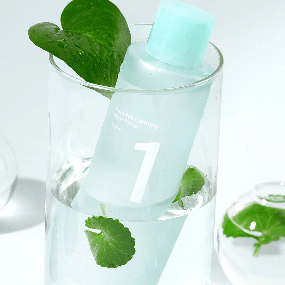 Butelka z No.1 Pure-Full Calming Herb Toner umieszczona w szklance z wodą i zielonymi liśćmi. Butelka ma jasnoniebieską zakrętkę i etykietę z napisem "Pure-full Calming Herb Toner" oraz "300ml". Produkt wygląda świeżo z wodą i roślinnością w tle, co daje uspokajające i naturalne odczucie.