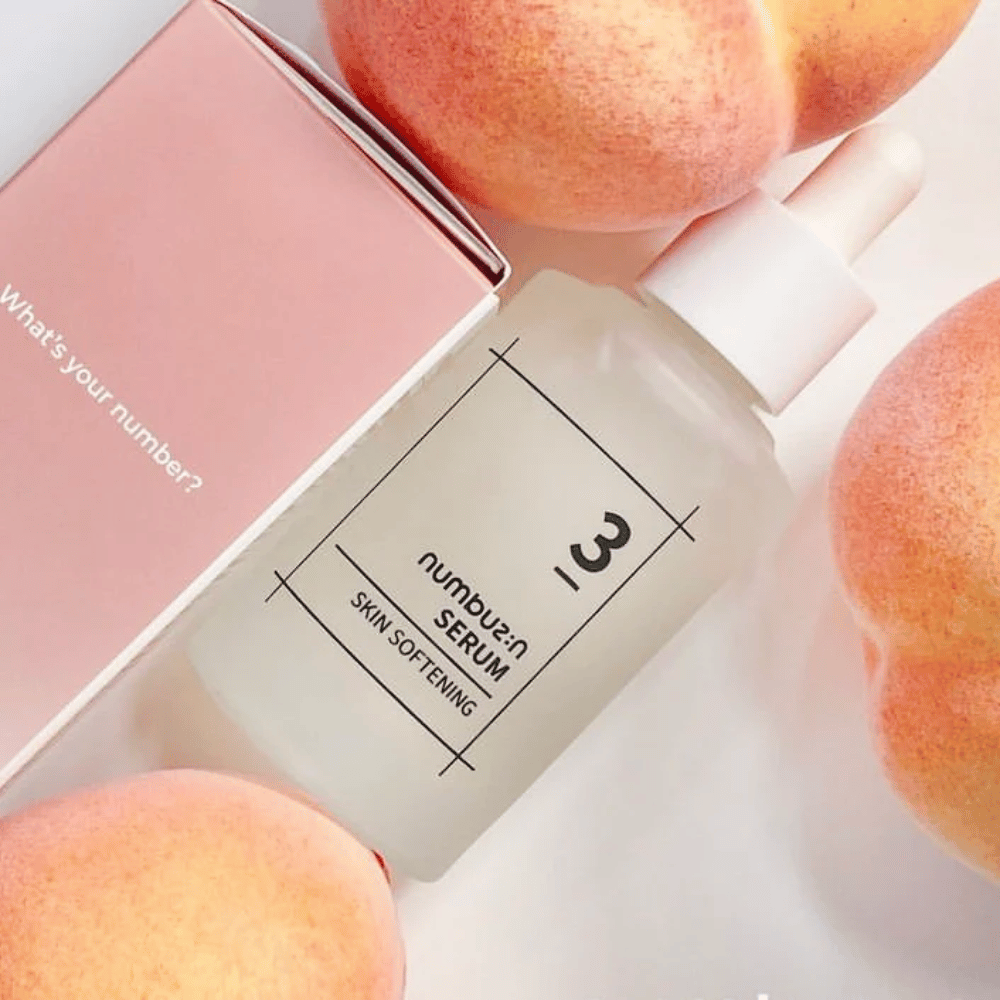 Butelka z numbus:in No.3 Skin Softening Serum otoczona brzoskwiniami i różowym pudełkiem z napisem "What's your number?".