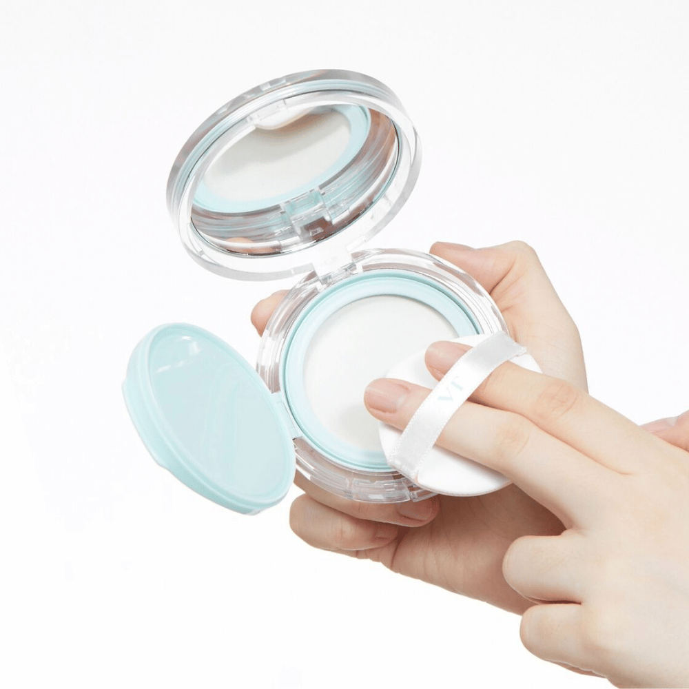 Ręka trzyma otwarty słoik z VT PDRN Essence Glow Sun Pact. Puszek jest gotowy do nałożenia pudru, który ma białą powierzchnię i niebieski brzeg wokół słoika.