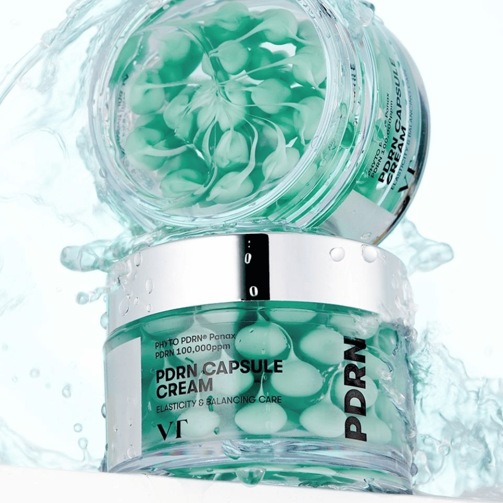 Dwa słoiki VT PDRN Capsule Cream ułożone w stos z rozpryskami wody wokół. Przezroczyste słoiki ukazują zielone kapsułki wewnątrz, z widocznym tekstem "Elasticity & Balancing Care" na etykiecie.