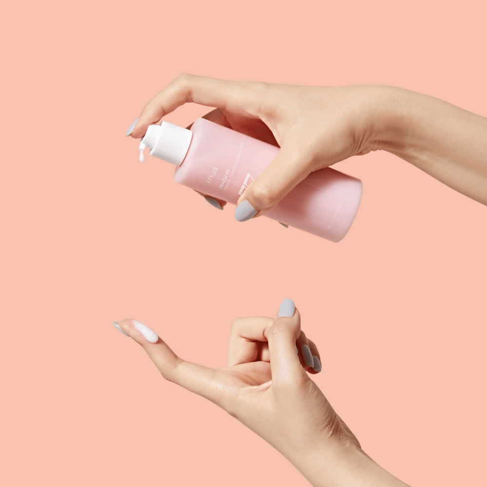 Obrazek przedstawia czyjeś ręce trzymające butelkę z ANUA Peach 77% Niacin Conditioning Milk. Ten produkt do pielęgnacji skóry wydaje się mieć mleczną konsystencję i jest zaprojektowany do pielęgnacji i poprawy stanu skóry.